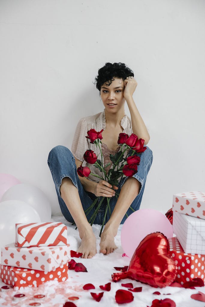 A Woman Sitting on Rug Holding a Bunch of Red Roses