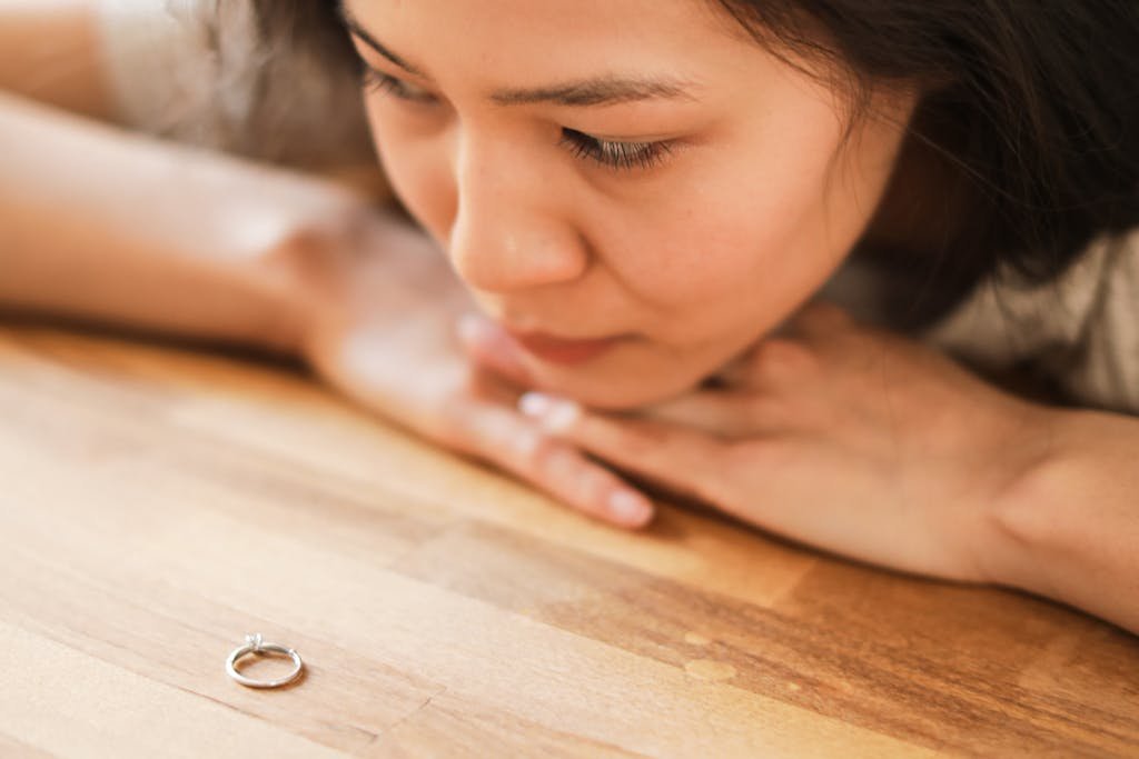 A woman in deep thought looks at a wedding ring on a wooden table, depicting contemplation or relationship doubts.